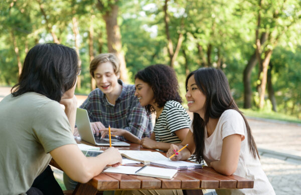 drie scholieren en een docent zitten buiten aan een picknickbankje te leren