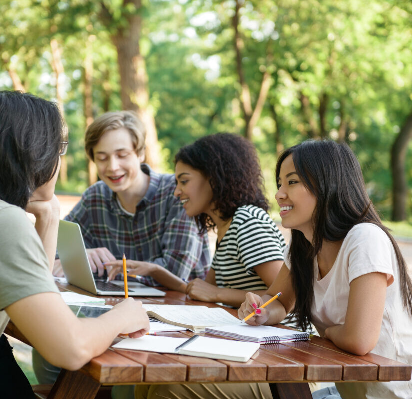drie scholieren en een docent zitten buiten aan een picknickbankje te leren
