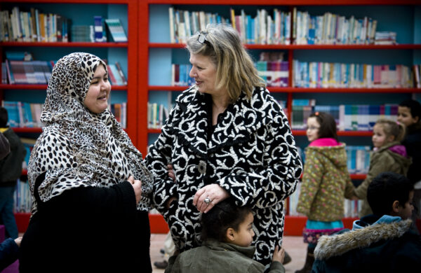 Twee leerkrachten in gesprek en kinderen.