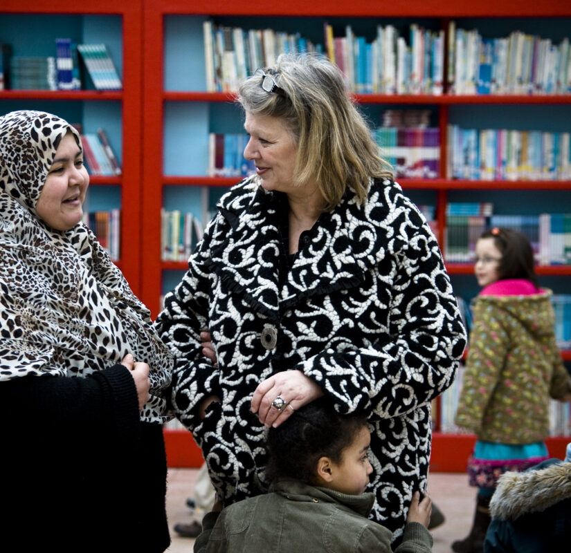 Twee leerkrachten in gesprek en kinderen.